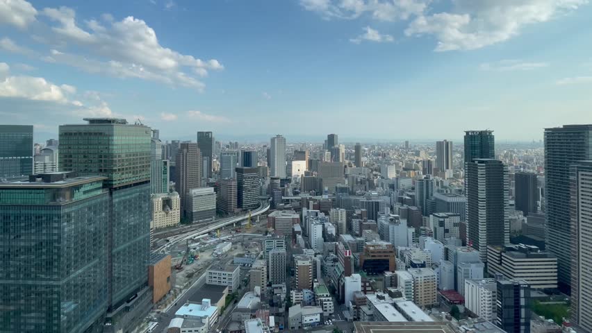 UMEDA, OSAKA, JAPAN - JUNE 2024 : Aerial high angle view around Osaka train station in daytime. View of crowded buildings at downtown area. Urban city and business concept video. Time lapse shot.