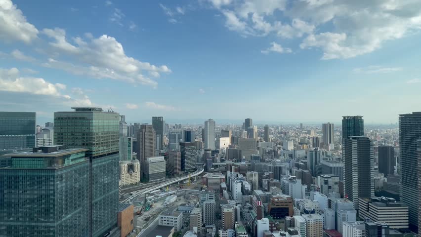 UMEDA, OSAKA, JAPAN - JUNE 2024 : Aerial high angle view around Osaka train station in daytime. View of crowded buildings at downtown area. Urban city and business concept video. Time lapse shot.