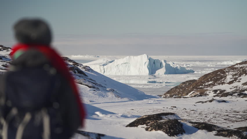 Adventurer gazing at a massive iceberg amidst Greenland