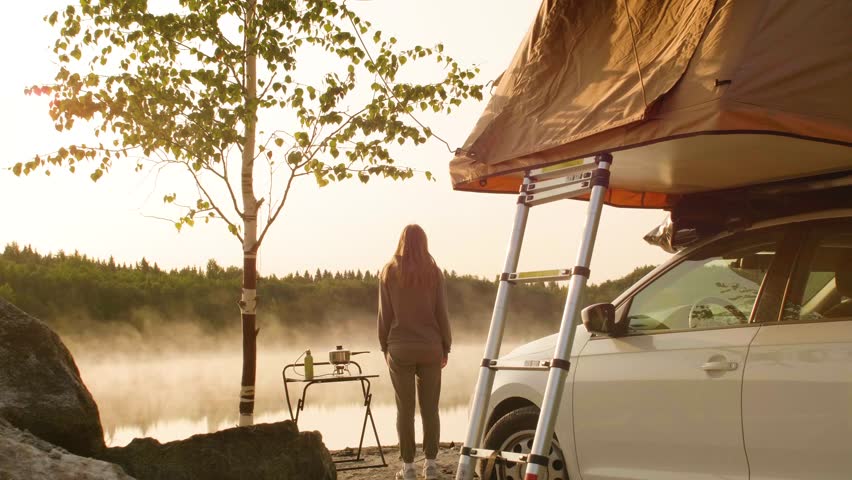 A woman standing on a lake shore and doing morning exercises at the campsite.