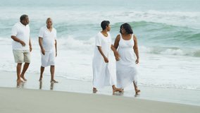 Two ethnic couples enjoying their retirement years strolling together on beach Travel and Tourism - Powered by Shutterstock - Get 15% off with code: PIKWIZARD15