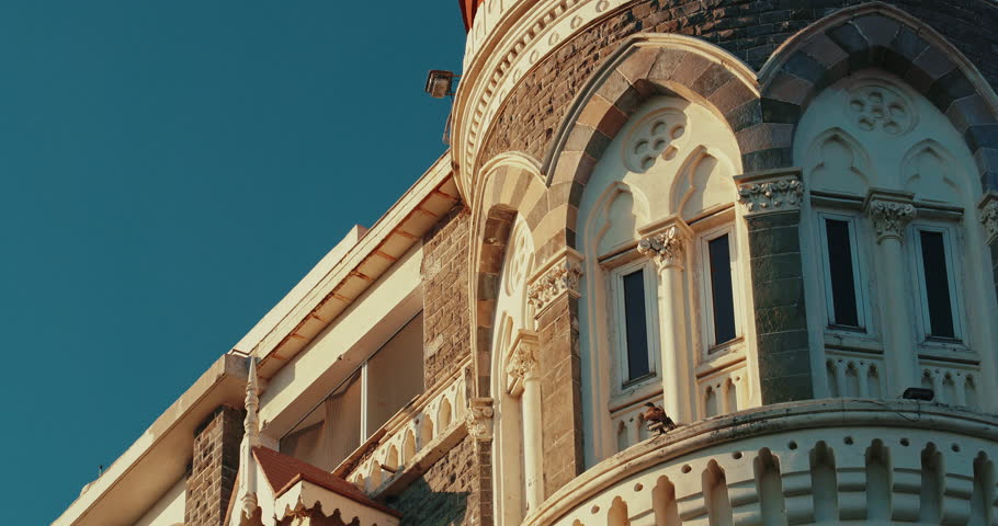 Mumbai, India. Flock Of Pigeons Fly In Slow Motion Above Taj Mahal Palace. Close-up View Black Kite Sit On Taj Mahal Hotel. Five-star, Luxury Hotel, Situated Next To Gateway Of India.