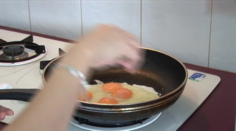 woman breaks egg and cooks scrambled eggs