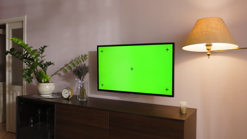 Modern living room scene featuring a television with a green screen placeholder, ready for custom content. TV is mounted on wall. Under screen there is wooden cabinet, accompanied by decorative items.