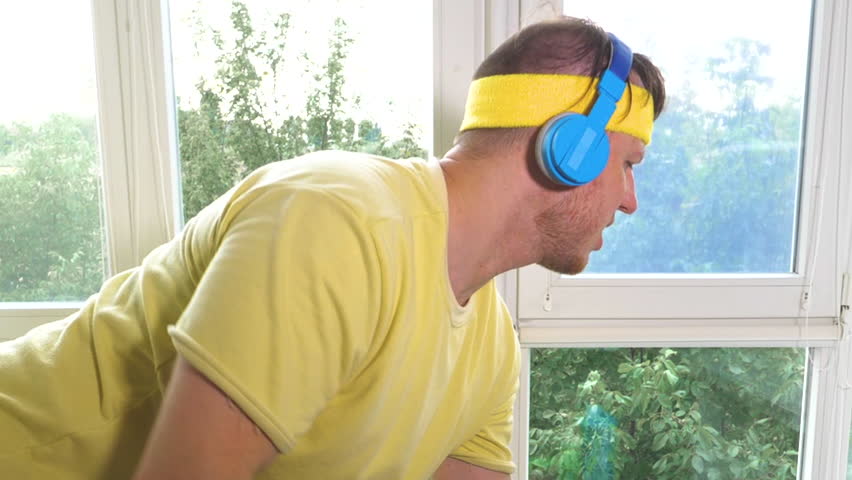 An athlete with dumbbells in his hands and wearing musical headphones while dancing. Home workout with dumbbells, pumping your back muscles. Slow motion