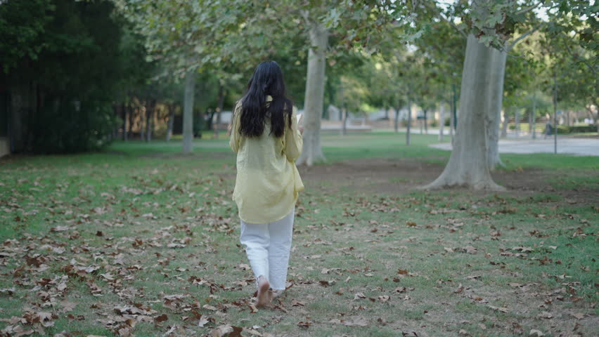 two young caucasian girls one brunette and one blonde walking and chatting barefoot on the grass towards camera while reading a book reading a book