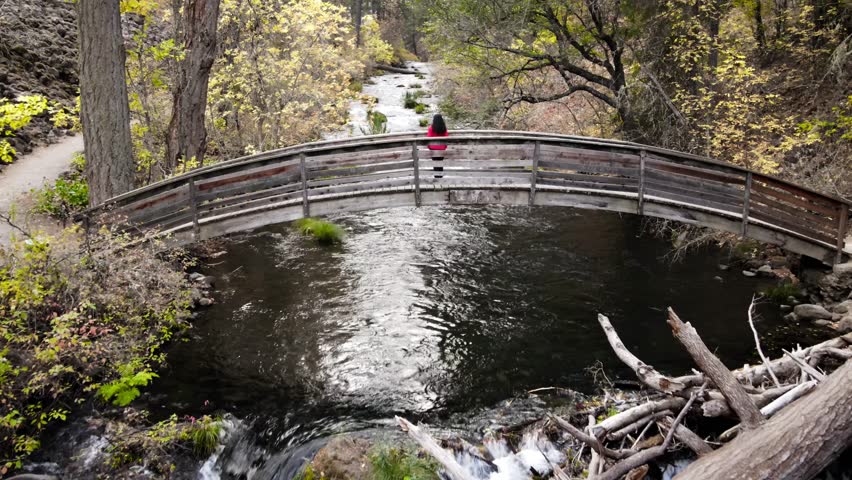 Aerial shot of a Asian female hiker walking across a bridge over Burney Creek in Northern California.