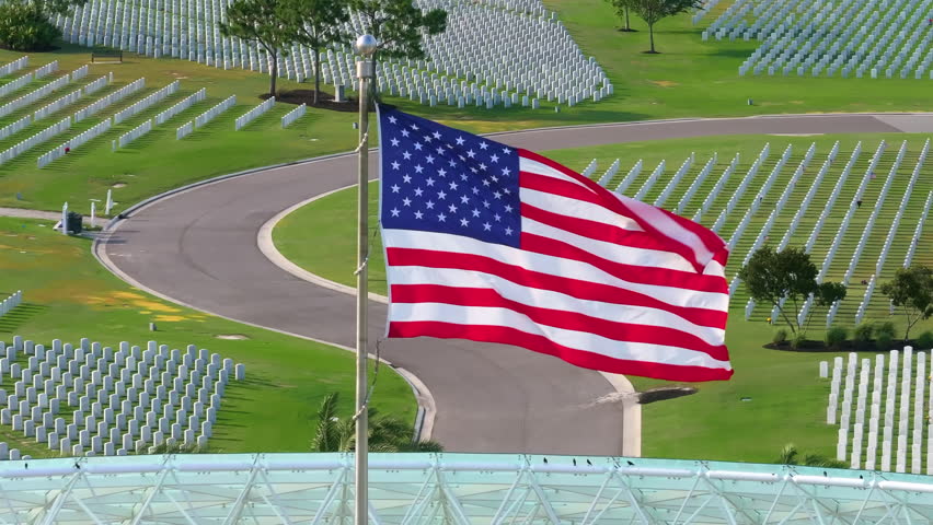 American army national cemetery with rows of white headstones and USA flag on green grass lawn. Memorial Day concept.