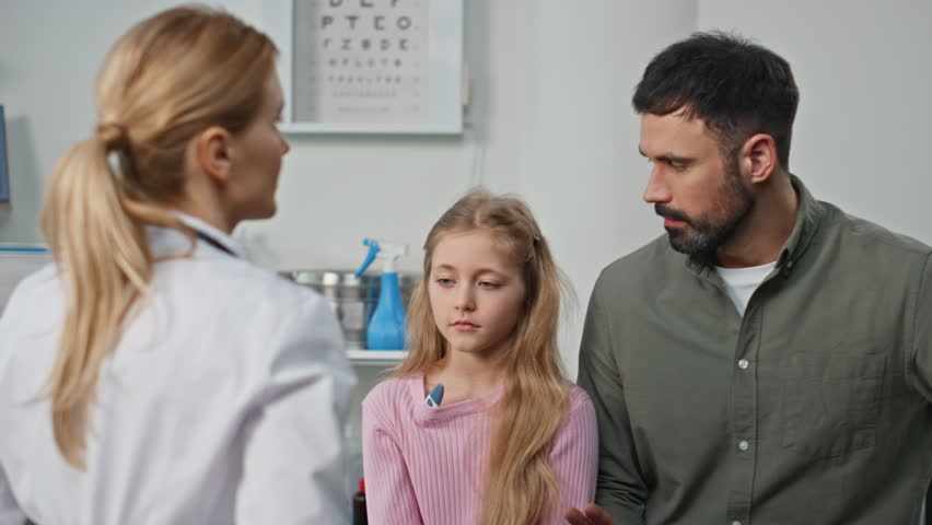Ill girl visiting clinic doctor with parent closeup. Pediatrician measuring body temperature discussing diagnosis symptoms in examination room. Serious father talking sick child during appointment. - Powered by Shutterstock - Get 15% off with code: PIKWIZARD15