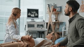 Expecting parents visiting ultrasound examination at clinic feeling excited. Professional doctor performing scan displaying fetus on monitor. Happy husband supporting wife during medical appointment - Powered by Shutterstock - Get 15% off with code: PIKWIZARD15