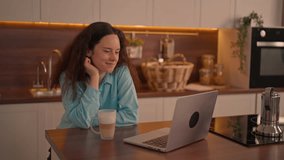 A woman sips her coffee and smiles at her laptop, surrounded by a well-decorated kitchen in a warm, inviting atmosphere. - Powered by Shutterstock - Get 15% off with code: PIKWIZARD15
