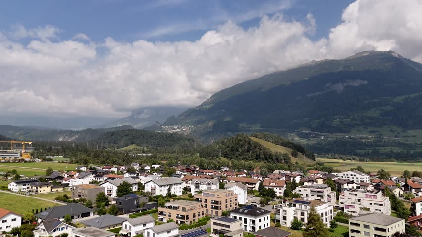 Modern residential apartment in swiss town of Bonaduz during summer day. Clouds and green mountain range in background. Slow forward shot.