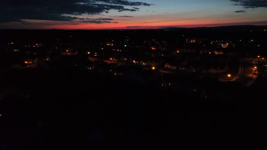 Aerial rising shot of illuminated city in America after golden sunset. Twilight scene at night. Orange lantern on street. Wide shot.