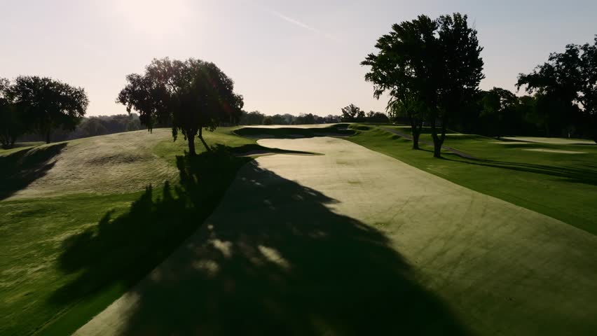 push in aerial drone shot down the fairway of a beautiful golf hole at a country club during sunrise