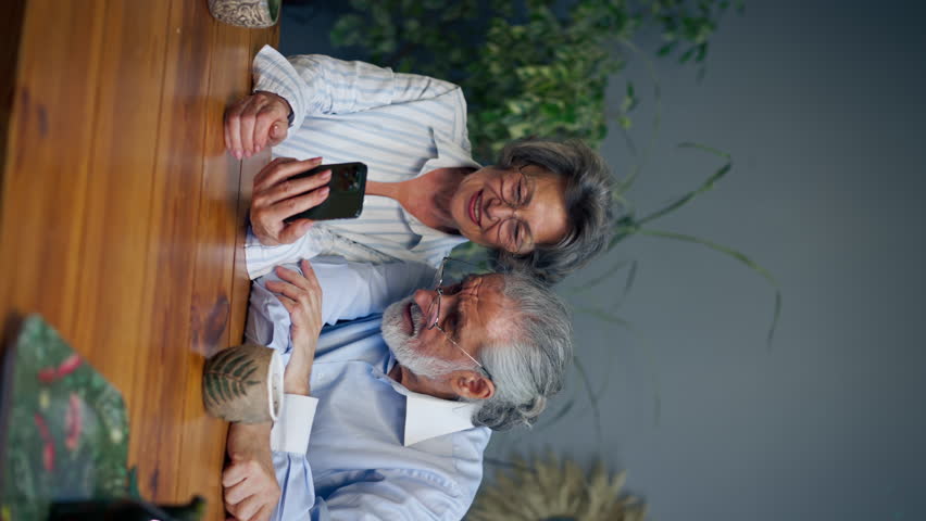 vertical video elderly people sitting at a table together watching social networks on the phone funny videos happy old age elderly couple pleasant memories leisure time in old age warm feelings