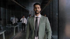 Self-confident business handsome adult man walks on way to office hallway crowded diverse colleagues. Attractive young successful executive in suit strolls staring at something with serious expression - Powered by Shutterstock - Get 15% off with code: PIKWIZARD15