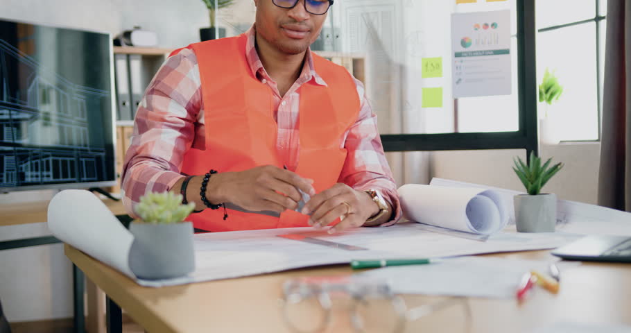 Man constructor in hardhat and vest drawing lines in building project working in modern design office