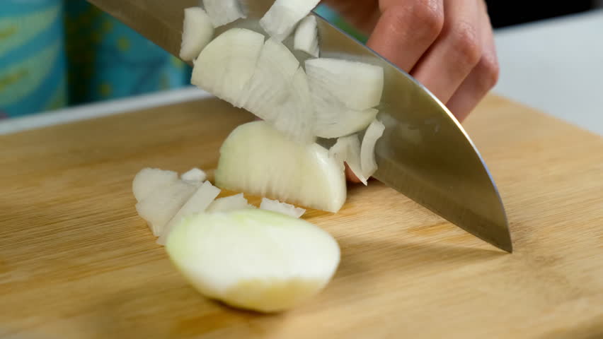 Hands of woman cutting onion on wooden board on slices using big knife for cooking salad, dish. Female preparing food from eco products, ingredients at home. Cuisine, culinary, recipe concept.