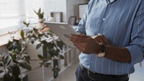 Side tilt shot of mature bearded Biracial businessman in glasses and striped blue shirt working on digital tablet at modern office, checking emails or developing new project - Powered by Shutterstock - Get 15% off with code: PIKWIZARD15
