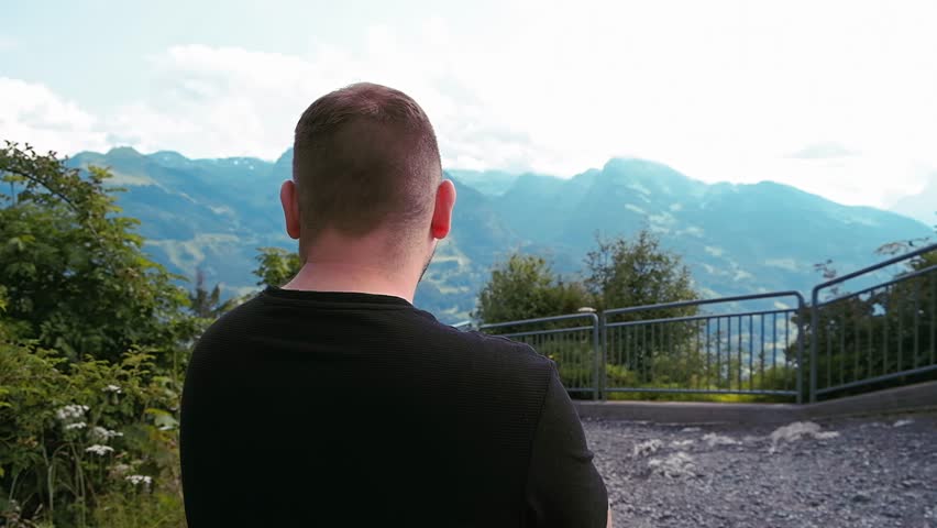 Man Gazing at Mountains: Back View. Solo Traveler Facing Majestic Mountains
