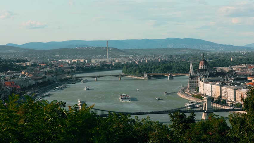 Budapest Hungarysunset panoramic view of the Danube River, Szechenyi Chain Bridge, and neo-Gothic Parliament at sunset. Cruise ships and commercial vessels navigate this major European waterway. This strategic capital hosts Prime Minister Viktor Orban