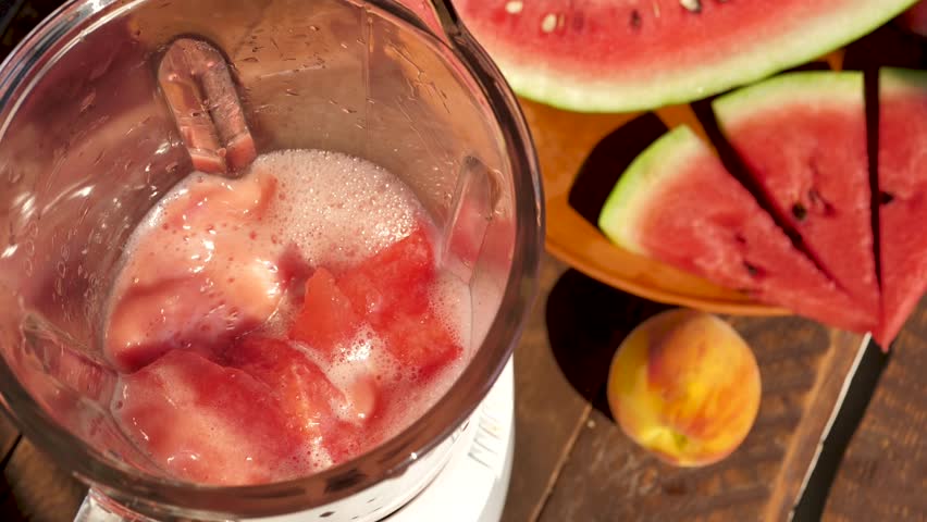 Top view of the process of mixing watermelon pulp with fruits in a blender. Making a watermelon fruit cocktail with a blender standing on a wooden table
