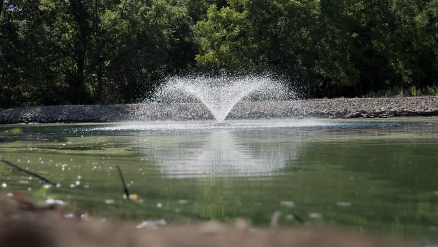 Slow motion of water fountain and sprout in the middle of a private property farm with a water line going underneath the lake into the center of the faucet