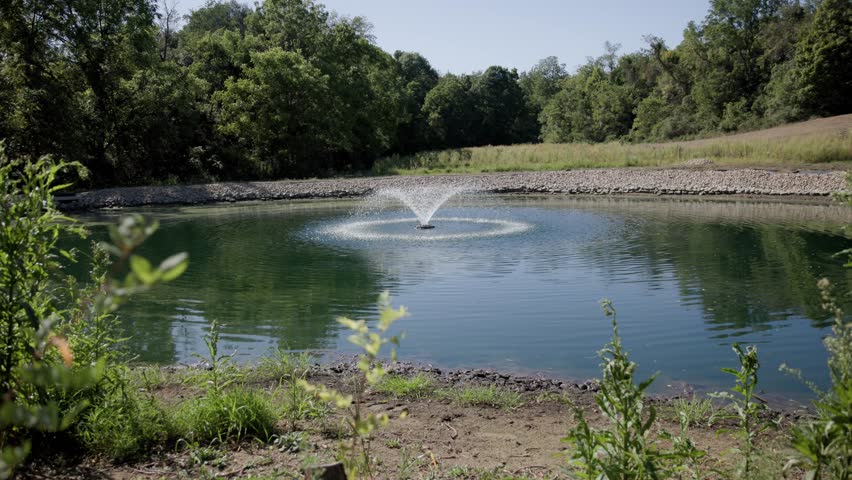 Slow motion of water fountain and sprout in the middle of a private property farm with a water line going underneath the lake into the center of the faucet