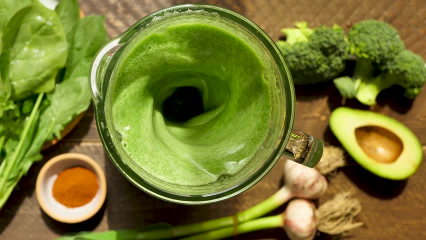 Top view mixing vegan smoothie using blender adding spinach leaves, avocado, broccoli and garlic. Make green smoothie to maintain vitamins in the body. Healthy vegan drink