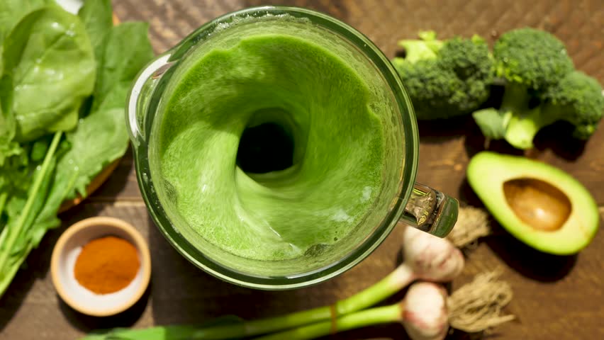 Top view mixing vegan smoothie using blender adding spinach leaves, avocado, broccoli and garlic. Make green smoothie to maintain vitamins in the body. Healthy vegan drink