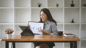 Confident Data Driven:  A young Asian businesswoman beams at a virtual meeting, showcasing positive growth charts on her tablet, in a bright, modern office setting.  - Powered by Shutterstock - Get 15% off with code: PIKWIZARD15