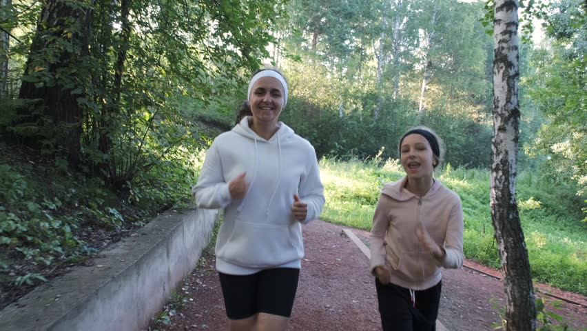 Young woman and her daughter happily jogging on a sunlit path at dawn, embracing nature and precious moments together. Healthy lifestyle concept