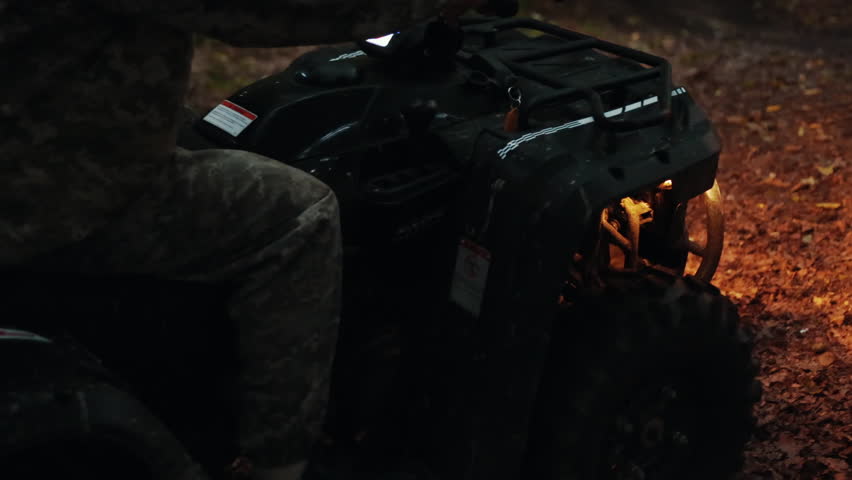 Headlight beam, ATV action, Muddy wheels. With headlights on, muddy ATV on dirt trail showcases rugged tires and front grille in close-up view.