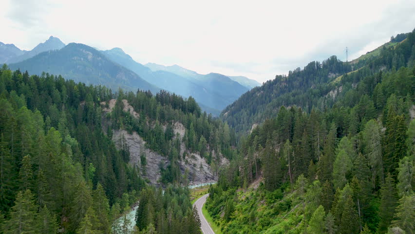 Scenic drone view of winding road through lush forested mountains in Montana during a cloudy summer day