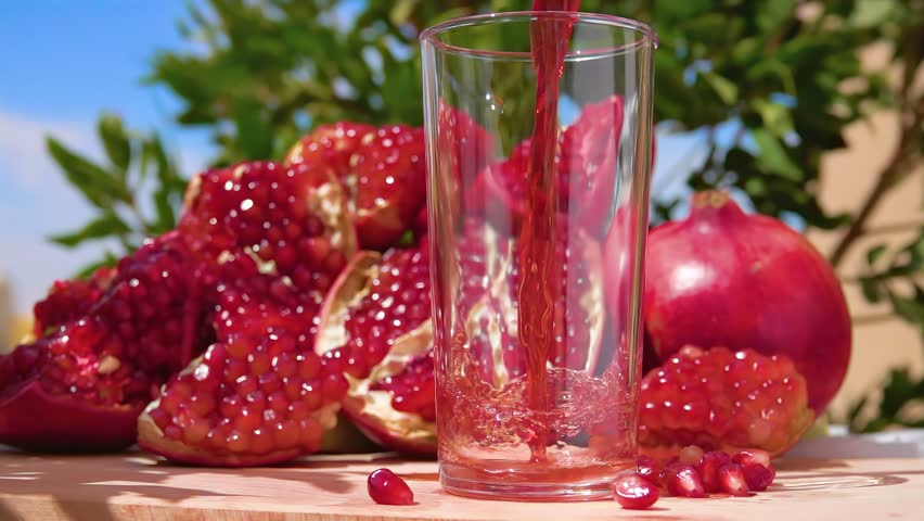 Freshly squeezed pomegranate juice wave is flowing into a jug in slow motion on the background of ripe pomegranate and blue sky