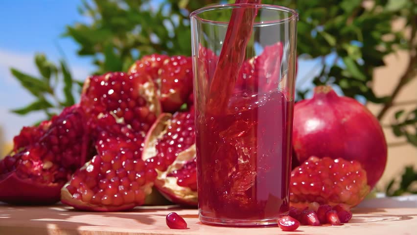 Freshly squeezed pomegranate juice wave is flowing into a jug in slow motion on the background of ripe pomegranate and blue sky