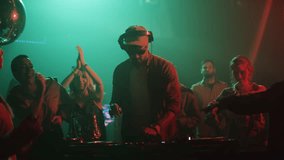 Handheld shot of a DJ playing music on mixer controller at disco club while young people dancing in the background. Slow-motion shot - Powered by Shutterstock - Get 15% off with code: PIKWIZARD15