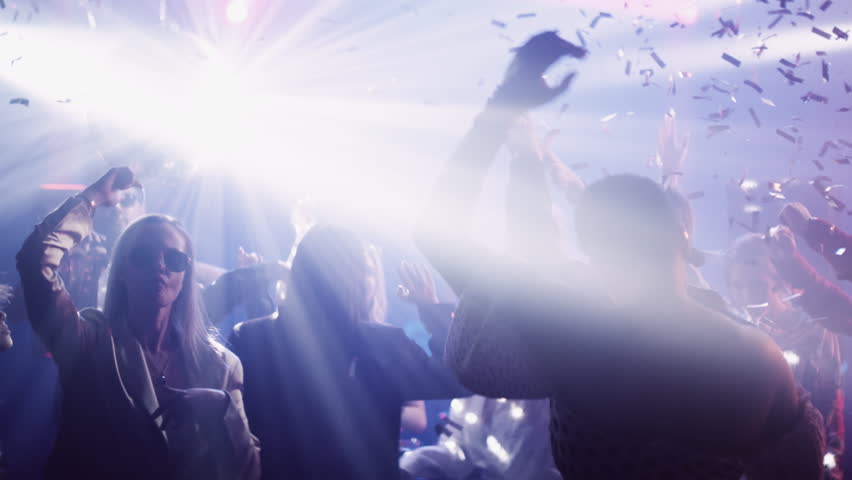 Group of friend celebrating and dancing in night club with illuminated neon night lights and falling confetti