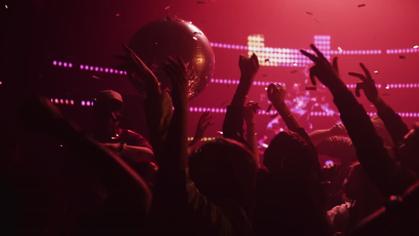 Extreme slow-motion shot of a group of people dancing happily with raised hands under falling confetti