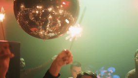Young multiracial group of people having fun with sparkle fireworks, celebrating Christmas and dancing in the discotheque. Large silver disco ball above the dance floor - Powered by Shutterstock - Get 15% off with code: PIKWIZARD15
