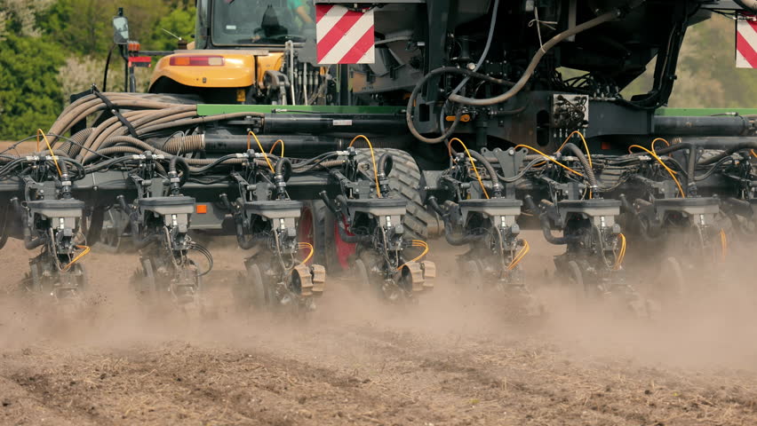 Close-up of seed drill in action in the field, A close-up shot of a seed drill operating in a field, with dust rising as it plants seeds into the soil.