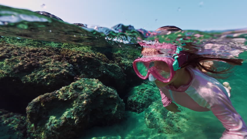 Girl child swims and snorkels under water. Kid dives into the ocean wearing goggles and looks at the underwater world. High quality 4k footage