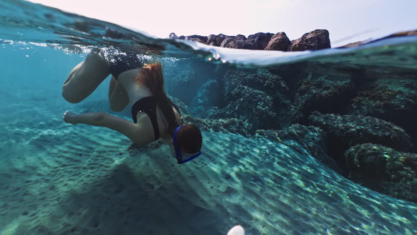 A beautiful girl in a mask for swimming under water dives into the ocean. Vacation at sea underwater world and reefs swimming with mask goggles. High quality 4k footage