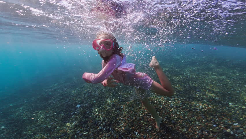 A baby girl dives and fools around underwater in glasses. Active recreation of swimming and snorkeling in the ocean. High quality 4k footage