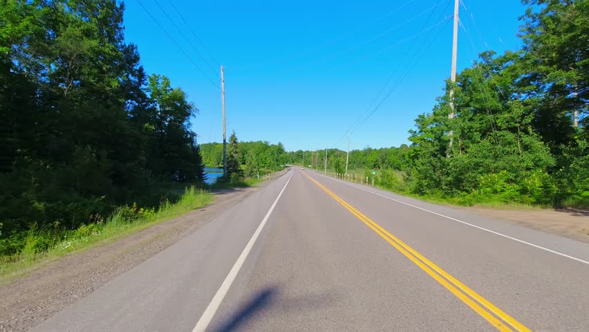 Driving POV Highway 28 passing rocky greenery between Bancroft and Kawartha, Ontario, Canada. Asphalt road through tall green forests. Driving plate from the back of the car point of view.