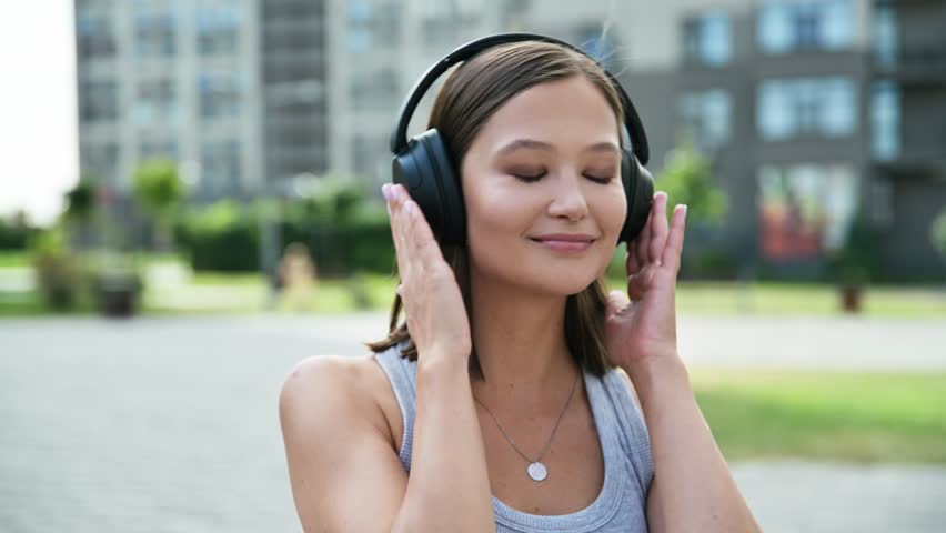 Happy beautiful young woman in headphones listening to music, outdoors