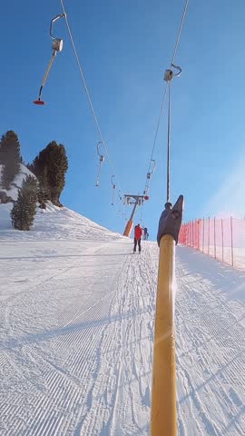 First-person view FPV point of view POV of cable chair ski lift ascend for alpine skiing in Dolomites. Ski resort piste with people skiing in Dolomites in Italy. Ski area Belvedere. Canazei, Italy