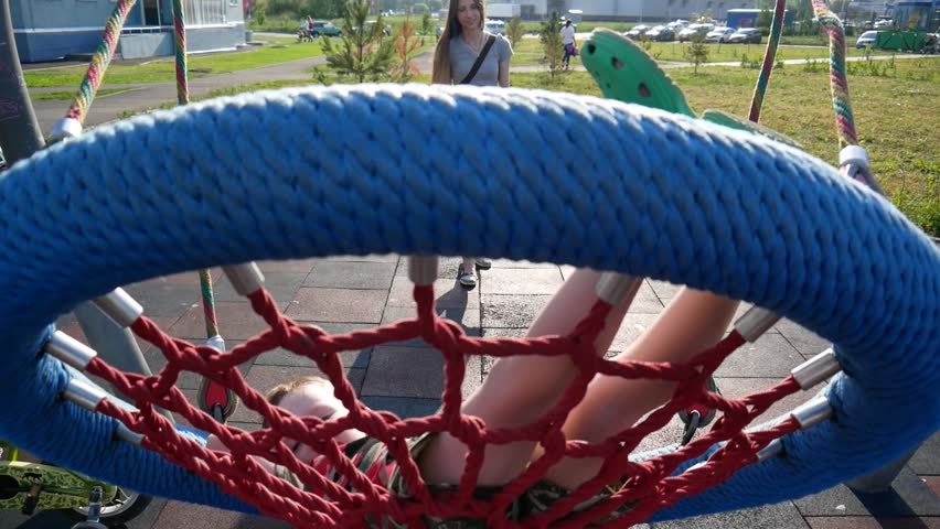 A young mother swinging a hammock swing with her little son
