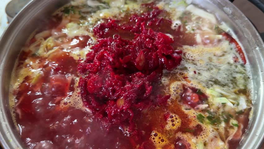 Boiling meat broth with potato, cabbage, saute carrots, beetroot and onions mix with tomatoes in a stainless steel pot during the borscht cooking, top view during stirring with a spoon
