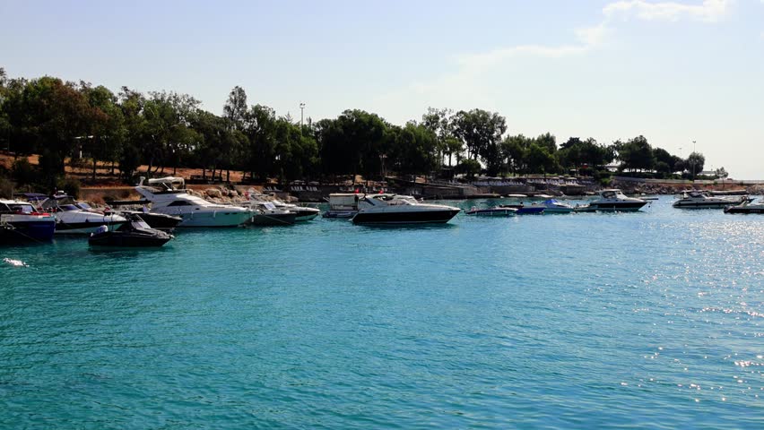 Sparkling water glistens under a clear blue sky, showcasing a tranquil scene with boats lined up at a marina, capturing the essence of a peaceful summer day